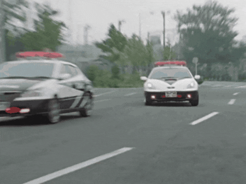 two police cars are driving down a street and one has a license plate that starts with the letter t
