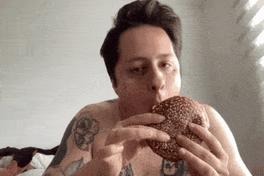 a man with a tattoo on his arm is eating a sandwich