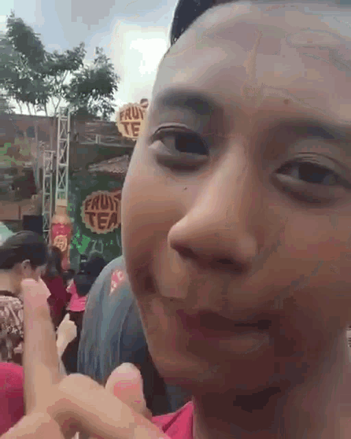 a young man making a funny face in front of a sign that says fruit tea