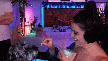 a woman wearing headphones is feeding a small dog while holding a drink .