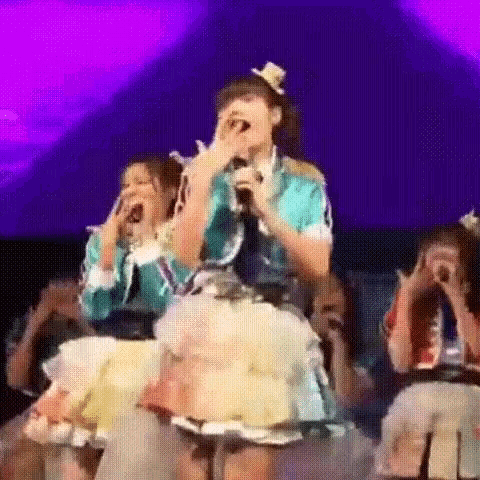 a girl is singing into a microphone on a stage while a group of people watch .