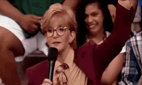 a woman with glasses is holding a microphone and raising her arm in the air .