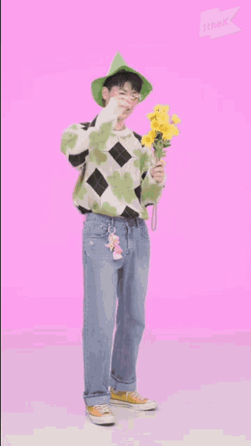 a young man wearing a green hat and a sweater is holding a heart shaped lollipop .