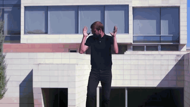 a man in a black shirt stands in front of a building with his hands in the air
