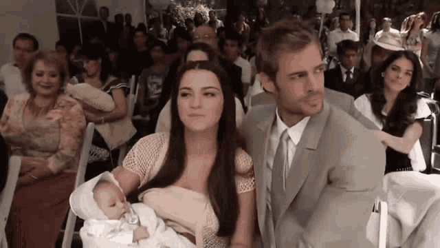 a man and woman are holding a baby in a crowded room