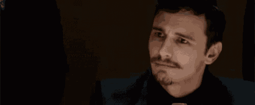 a man in a suit and tie is making a funny face while looking at his watch .