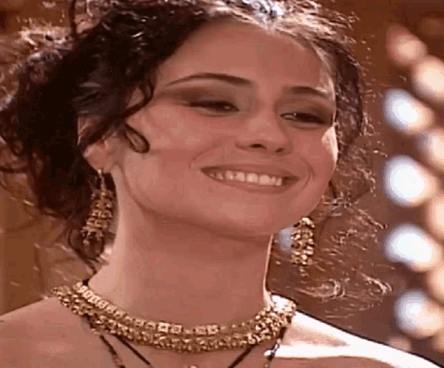 the woman is wearing a necklace and earrings and smiling .