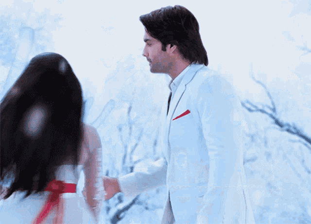 a man in a white suit and a woman in a white dress are hugging in the snow