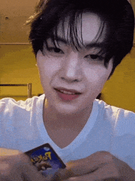 a young man in a white shirt is holding a pokemon card in his hand .