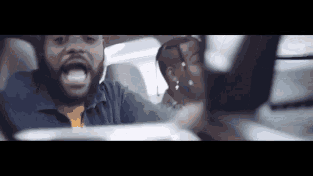a man with a beard is driving a car and shouting
