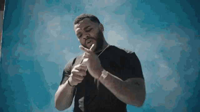 a man in a black shirt is standing in front of a blue background .