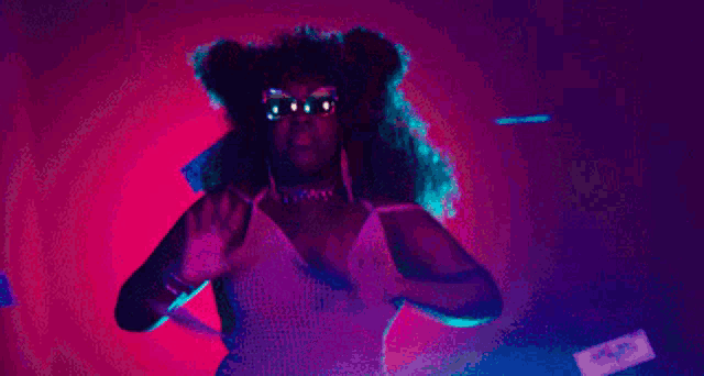 a woman with curly hair and glasses is dancing in a pink and purple light