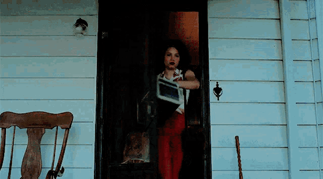 a woman in red pants is standing in a doorway holding a box