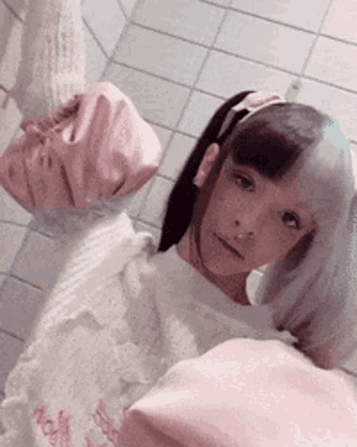 a girl with half black and half white hair is taking a selfie in a bathroom with a pink bag .