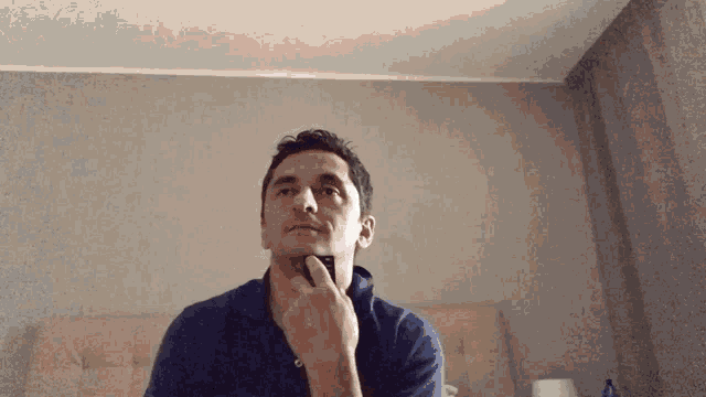 a man in a blue shirt shaves his face with a razor