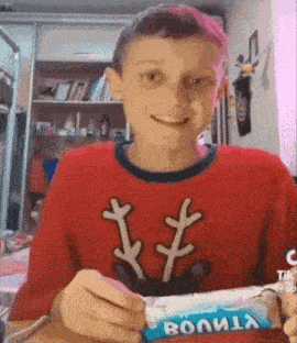 a young boy in a red sweater is smiling while holding a bar of candy