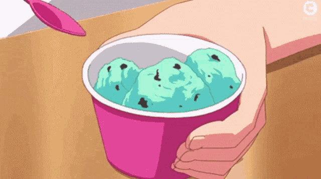 a person is holding a cup of mint chocolate chip ice cream with a spoon in it .