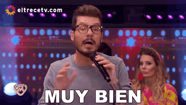 a man with glasses is holding a microphone and saying " muy bien "