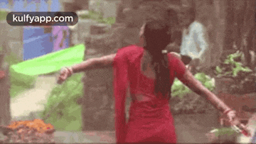a woman in a red saree is dancing in the rain .