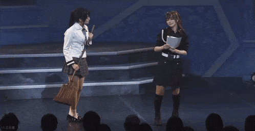 two women standing on a stage with one holding a broom and the other holding a piece of paper