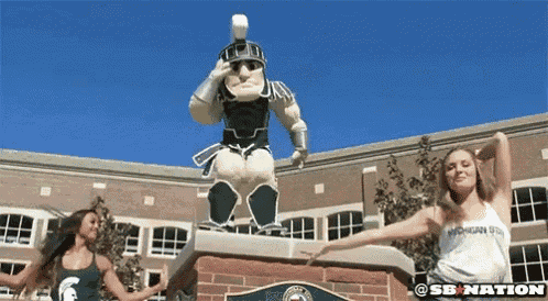 two women are dancing in front of a statue of a spartan soldier