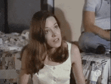 a woman in a white tank top is sitting on a bed .