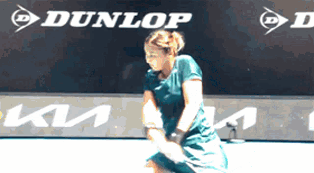 a woman is playing tennis in front of a dunlop ad
