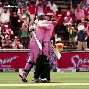 two cricket players in pink uniforms are hugging each other on the field .