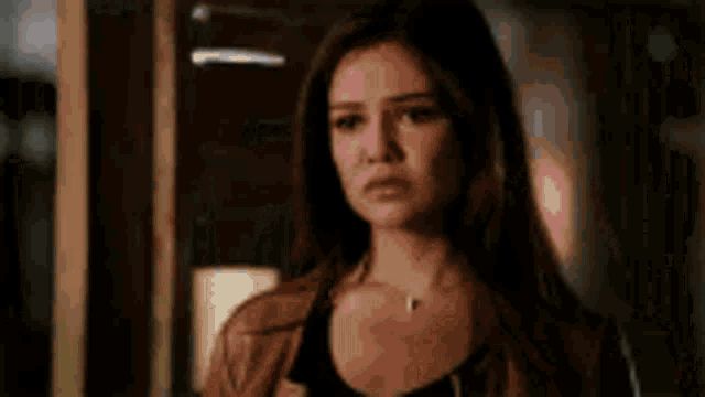 a woman with long brown hair is standing in a dark room looking at the camera .