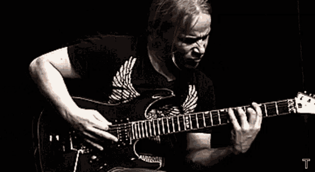 a man in a black shirt playing a guitar with the letter t in the corner