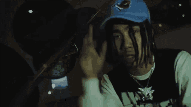 a young man with dreadlocks is wearing a blue hat and a white shirt .