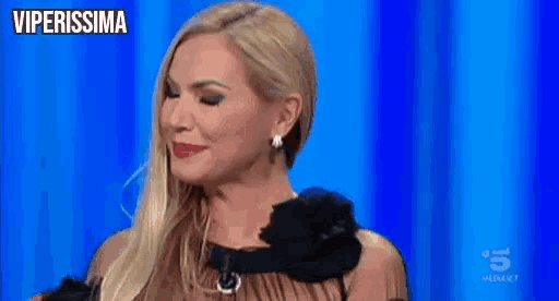 a woman wearing a black dress and earrings is sitting on a blue stage .