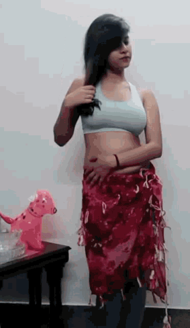 a woman in a white bra and a red skirt is standing next to a table .