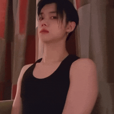 a young man in a black tank top is standing in front of a curtain .
