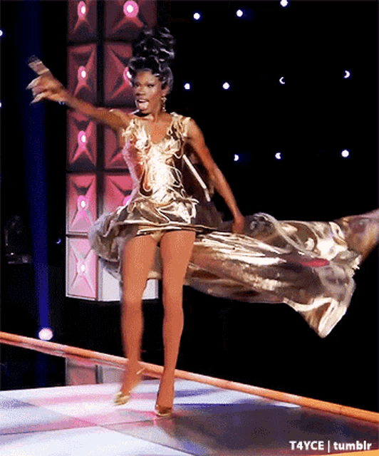 a woman in a gold dress is walking down a stage