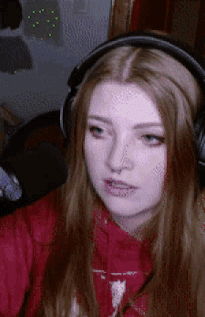 a woman wearing headphones and a red hoodie is making a face