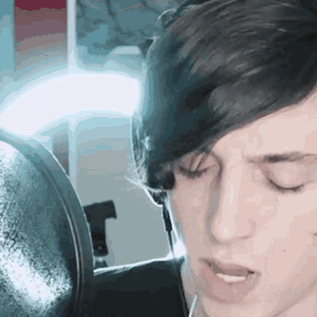 a young man is singing into a microphone in front of a mirror .