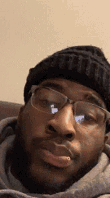 a man wearing glasses and a beanie is making a face .