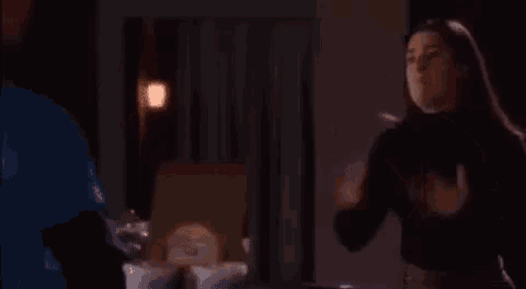 a woman is standing in a dark room with her hands on her chest and a man is standing behind her .