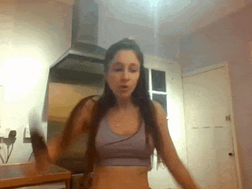 a woman in a purple sports bra is standing in a kitchen .