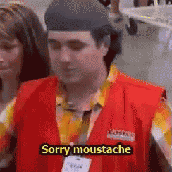 a man in a red vest says sorry moustache in front of a group of people