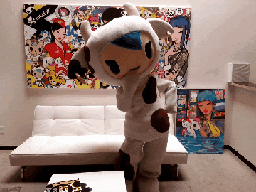a person dressed in a cow costume is standing in front of a painting that says tokidoki