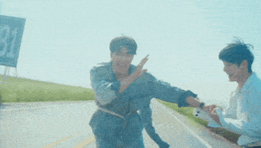 a man reaches out to help another man on a road with a b1 sign in the background