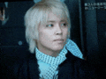 a man with blonde hair and a scarf around his neck is sitting in a dark room .