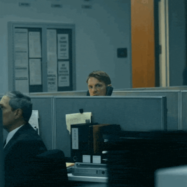 a man sits in an office cubicle with a binder labeled " aaoc " on it