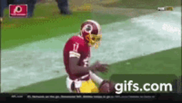 a football player wearing a red helmet is kneeling on the field .