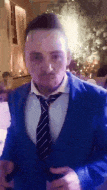 a man wearing a blue suit and tie is holding a glass of wine