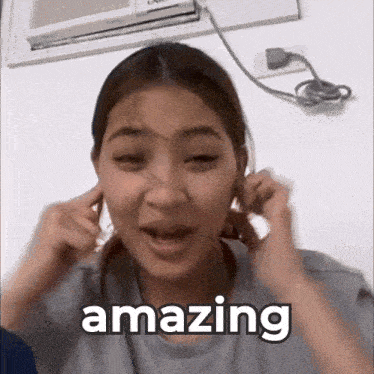 a woman is covering her ears with her hands and the word amazing is next to her .