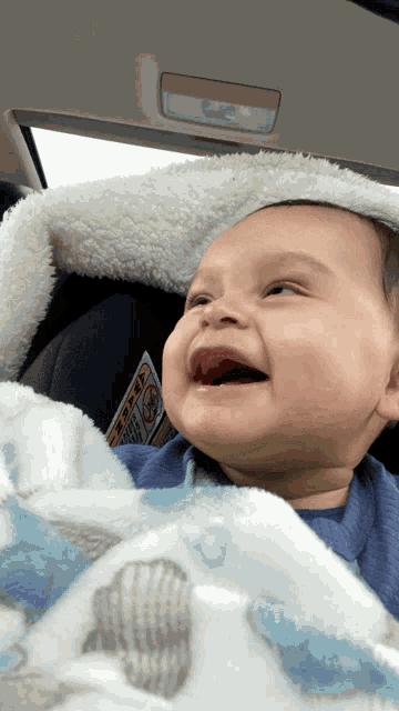 a baby is smiling while sitting in a car seat with a warning sign on the back