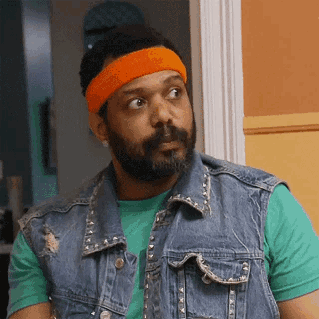 a man wearing a denim vest and an orange headband